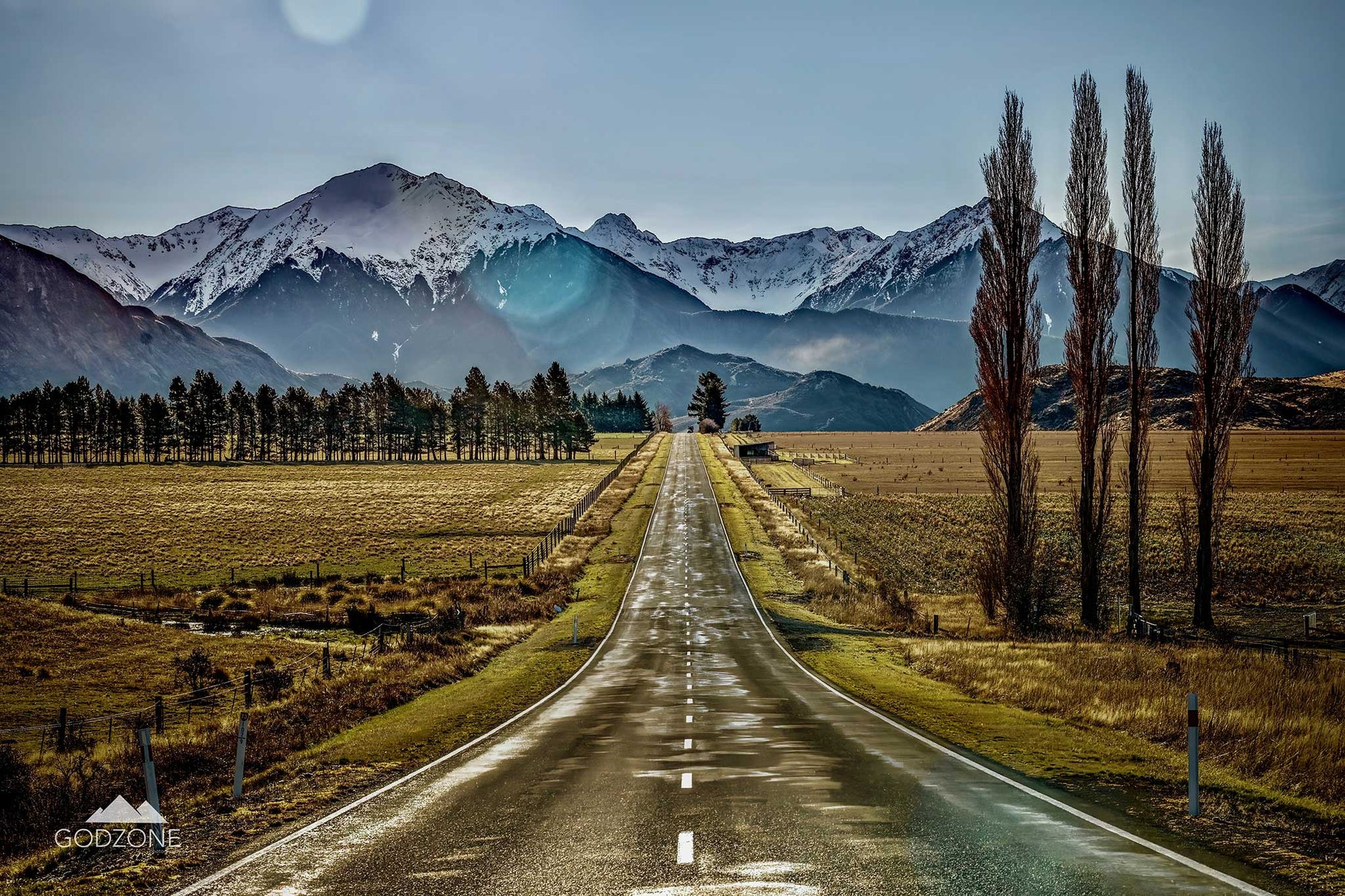 Inviting landscape photograph of the long, straight highway leading to Arthur's Pass with golden fields and snow-topped mountains. NZ South Island landscape photography for sale.