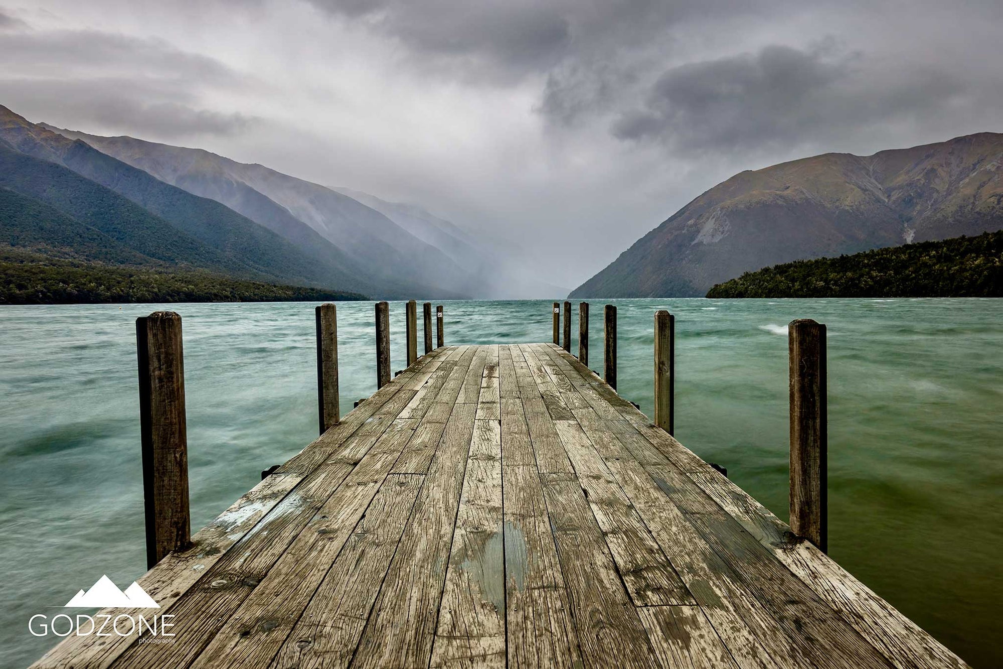 Striking landscape photograph of a wharf leading us into Lake Rotoiti in New Zealand's Bay of Plenty. Stunning green and misty hill atmospheric landscape photography NZ.