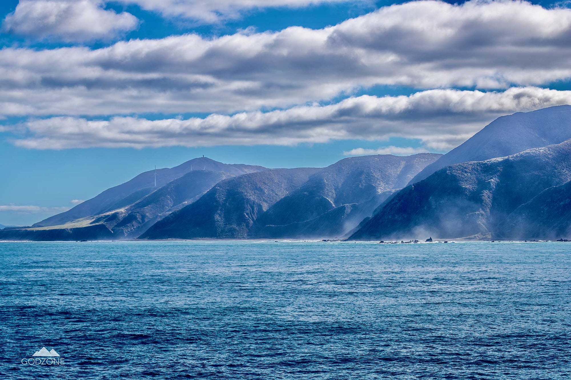 Beautiful landscape photograph of misty fiords along the Cook Strait in New Zealand with low-hanging clouds. Sapphire blue colour tones.