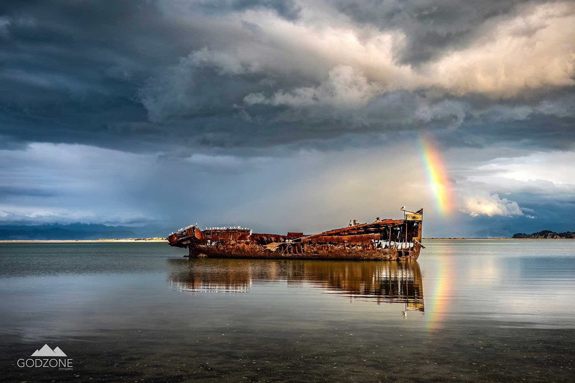 NZ seascape photograph of shipwreck in Motueka, rainbow above, stormy skies. NZ rusty metal artwork. 