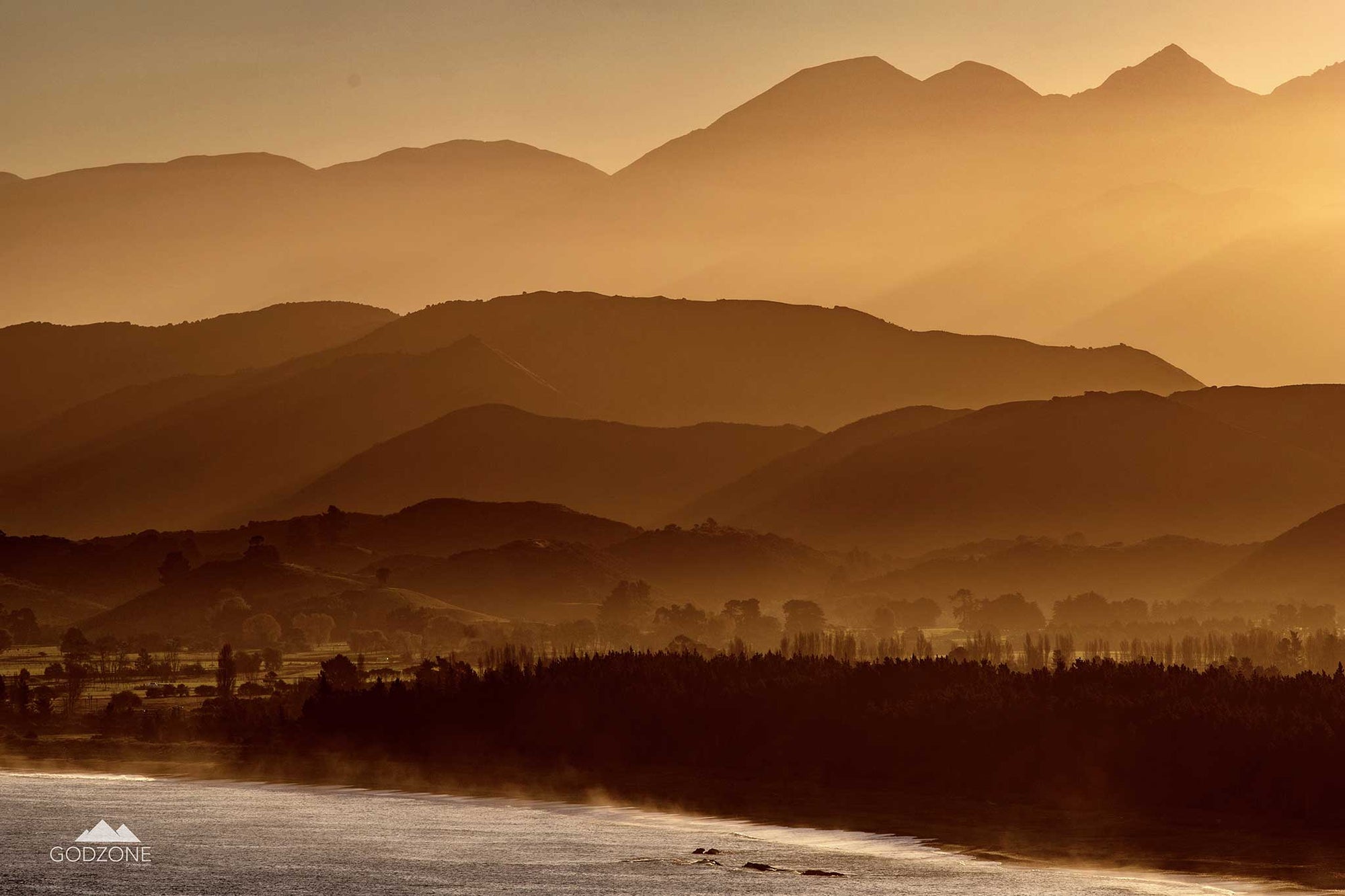 Subtle photograph showing layers of mountains, soft golden light falling, sea at the bottom. NZ gold interior design artwork. 