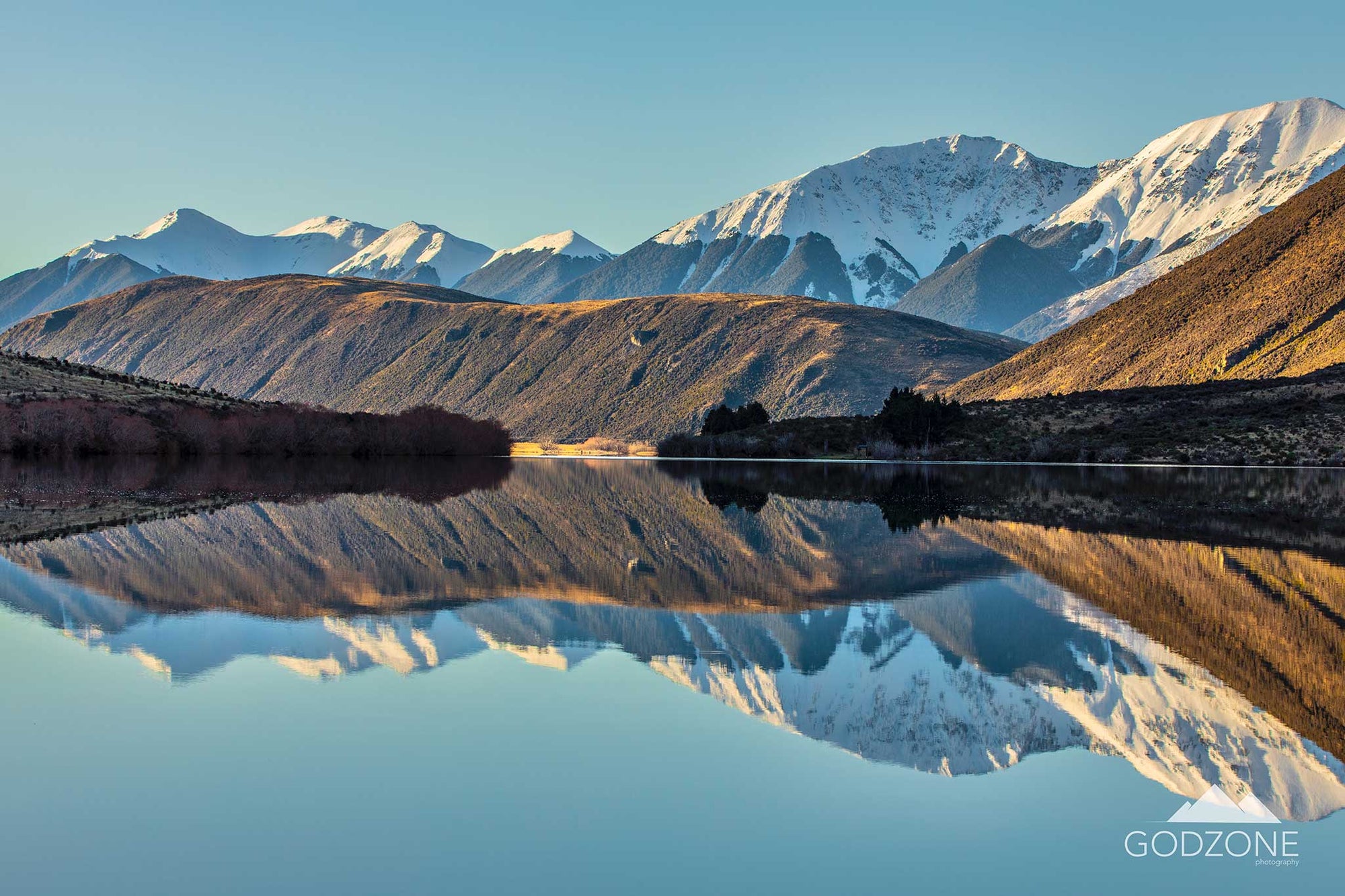 Beautiful reflective lake photograph showing snowy and golden mountains mirrored in Lake Pearson, Arthurs Pass. Periwinkle or sapphire blue NZ artwork for your wall.