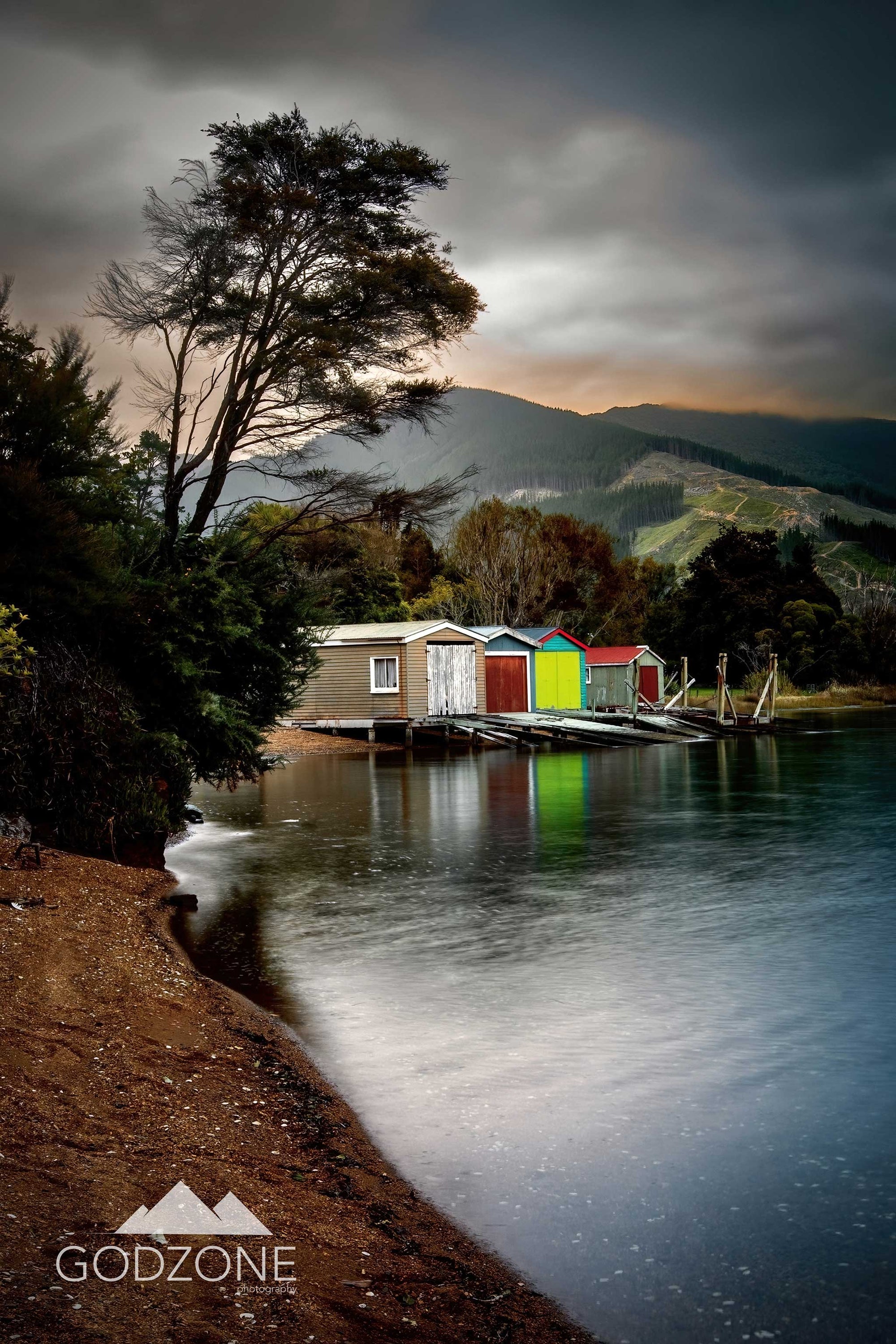 Tall portrait photograph of brightly painted boat sheds on the water at the grove in the Marlborough Sounds, Queen Charlotte. NZ boat house photography.