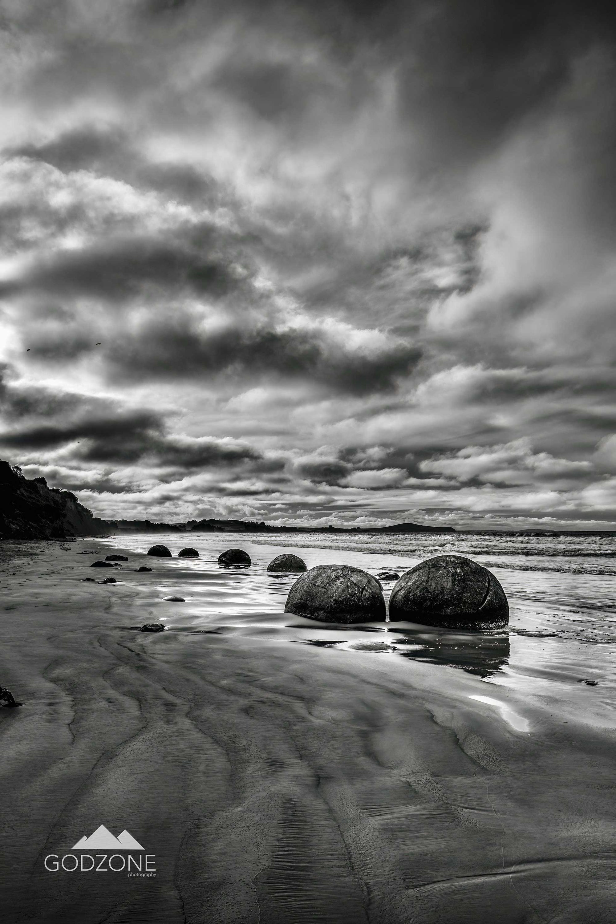 Black and white or greyscale landscape photograph of the Moeraki Boulders in the South Island, New Zealand. Buy tall portrait landscape photograph. 