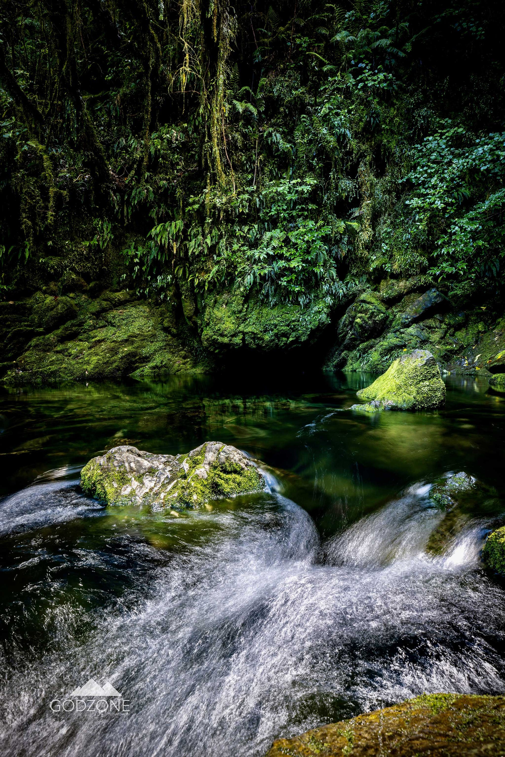 Beautiful NZ landscape photograph of long-exposure water falling over mossy stones in Riwaka, South Island, New Zealand. Tasman District.