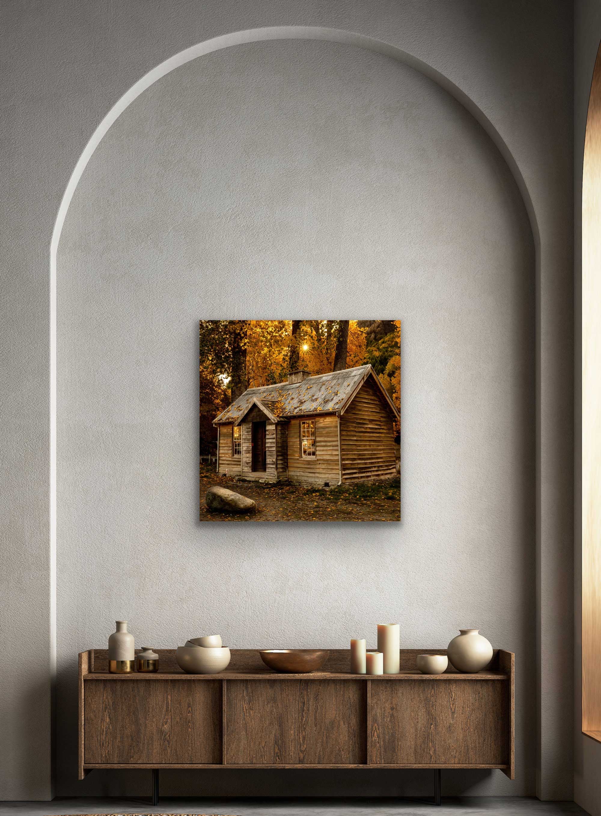 See Arrowtown house square photograph in situ. On wall above cabinet. Autumn photo of a wooden house with golden light through trees.