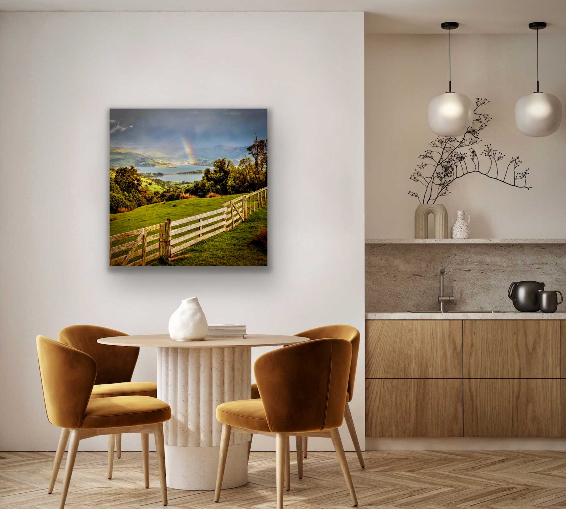 See banks peninsula photograph in situ, hung over a dining table with kitchen. Photo view from above, looking down on a small rainbow forming over the water. South Island, New Zealand.