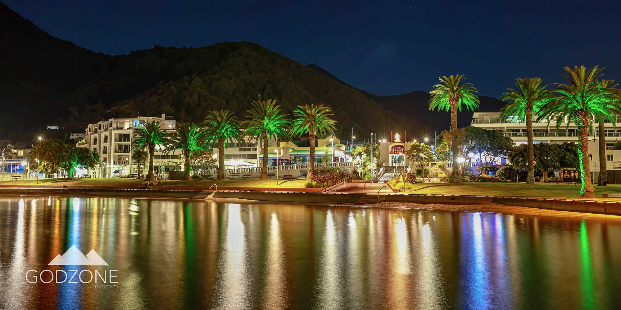 Stunning cityscape photograph of Picton harbour with reflected lights in the water and palm trees. NZ scenic photography for sale.