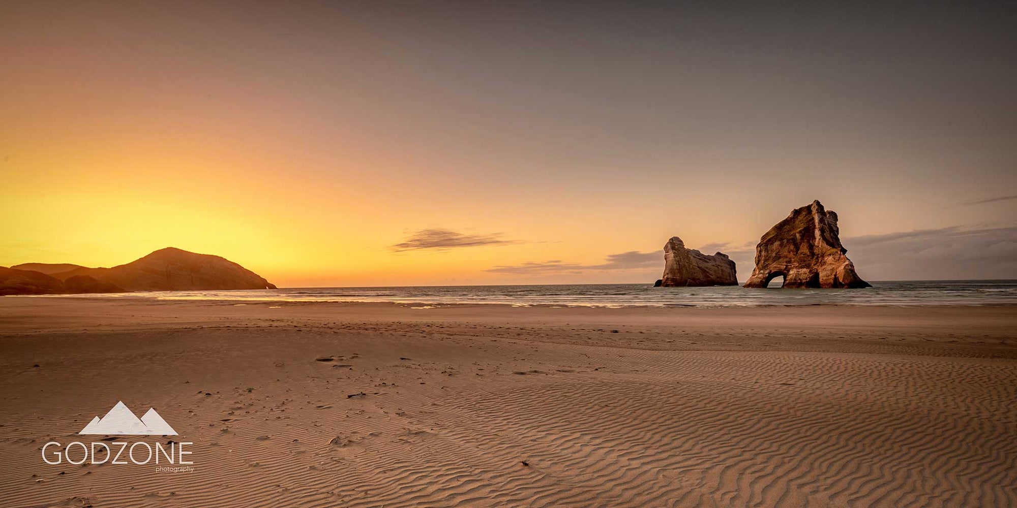 Sunset at Wharariki Beach photograph with soft yellow light and rock formations. Pale, subtle colours.